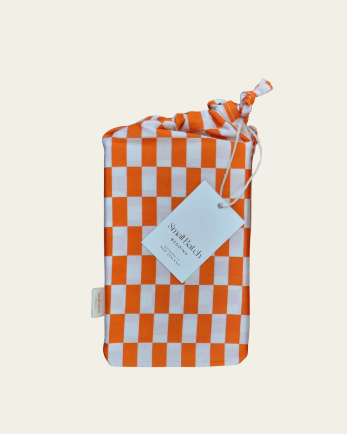 Tomato red orange and light checkered cotton product bag with a Small Batch Bedding tag on a light beige background.