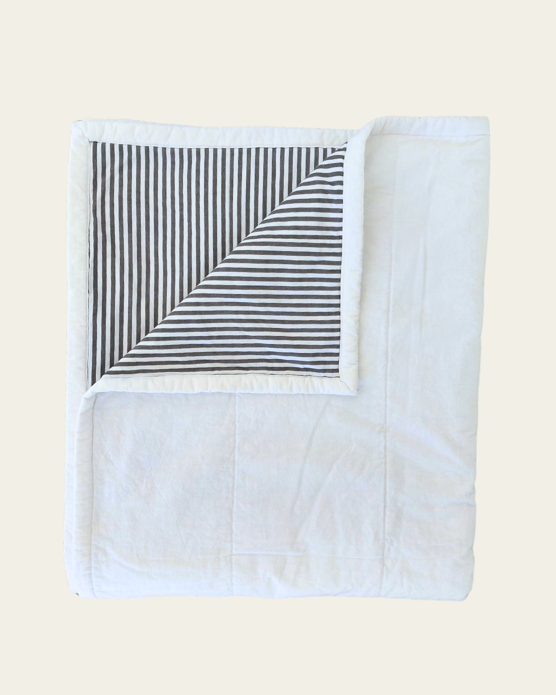 White quilt blanket with black and white striped inner corner on a beige background