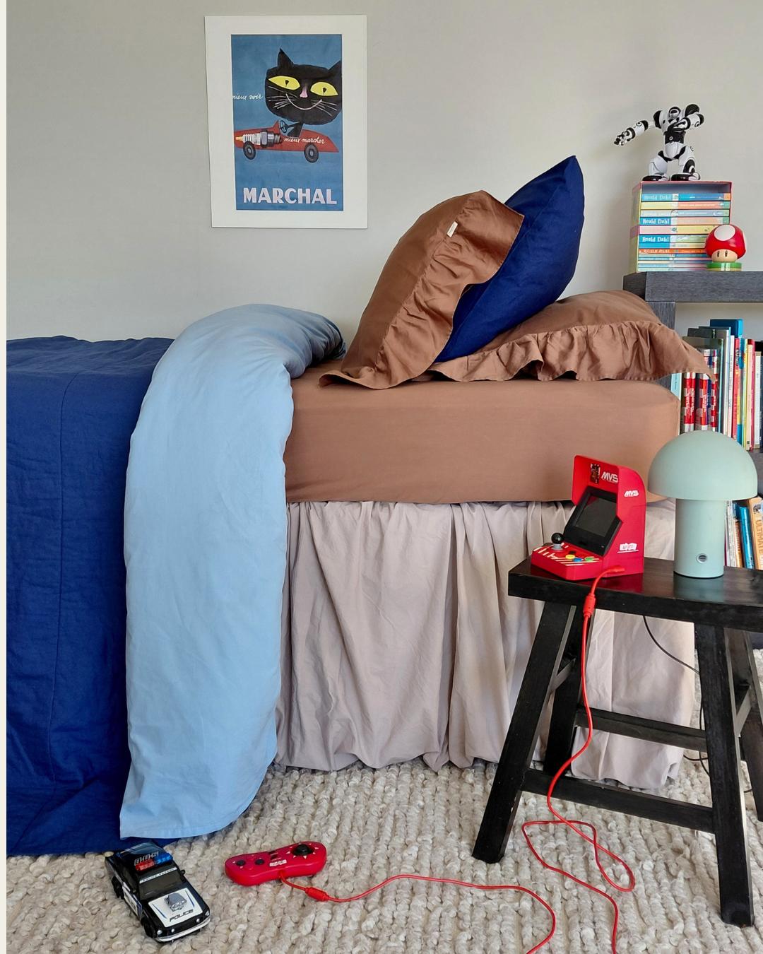 Children's bedroom with a bed with a chocolate brown fitted sheet and chocolate brown one sided ruffle pillowcases, toys, and books.