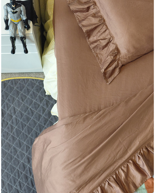 Chocolate brown fitted cotton sheet set on a bed with a superhero toy in the background.
