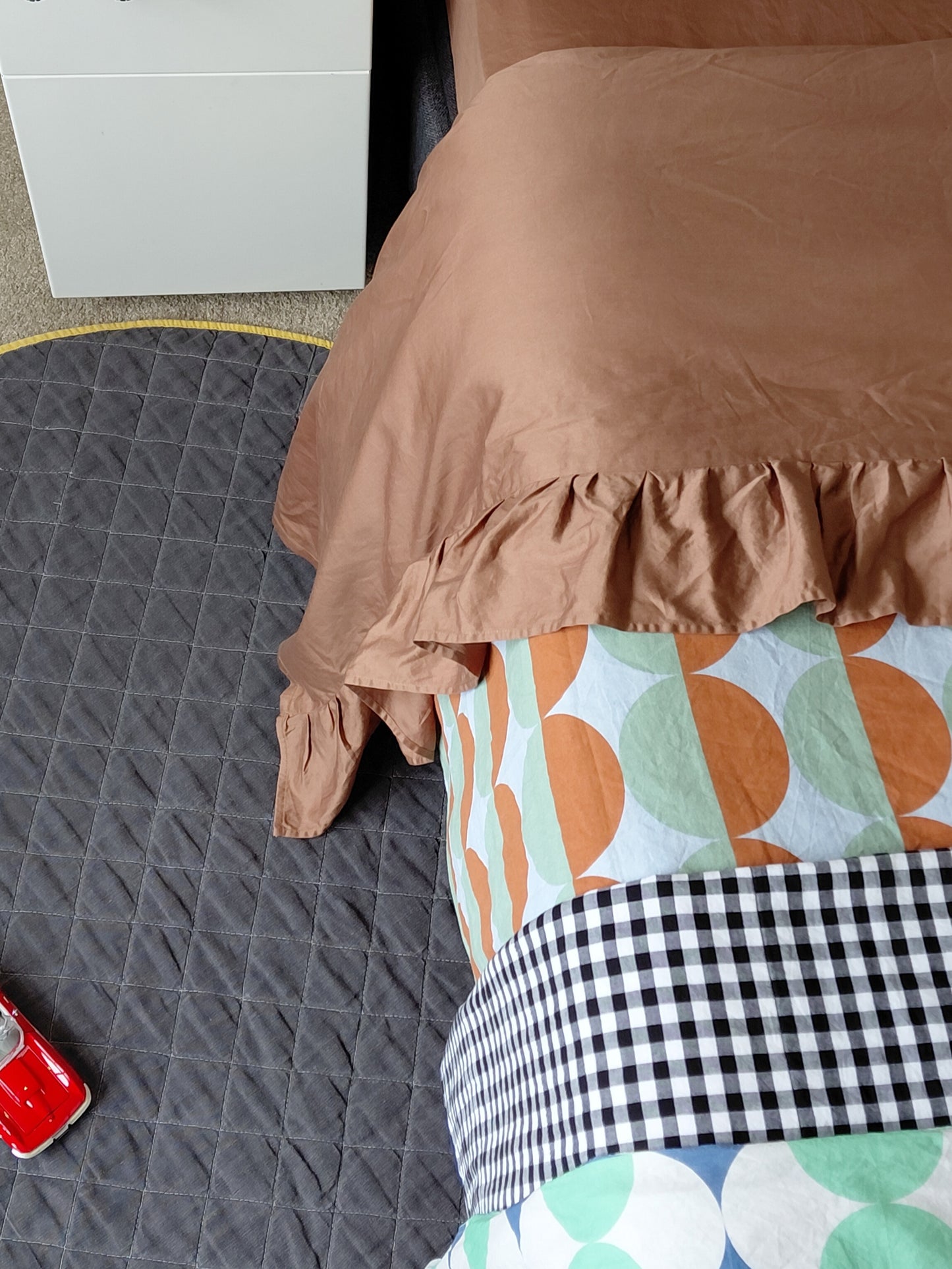 Brown chocolate top sheet with ruffle draped over a child's bed with a colorful patterned rug underneath.