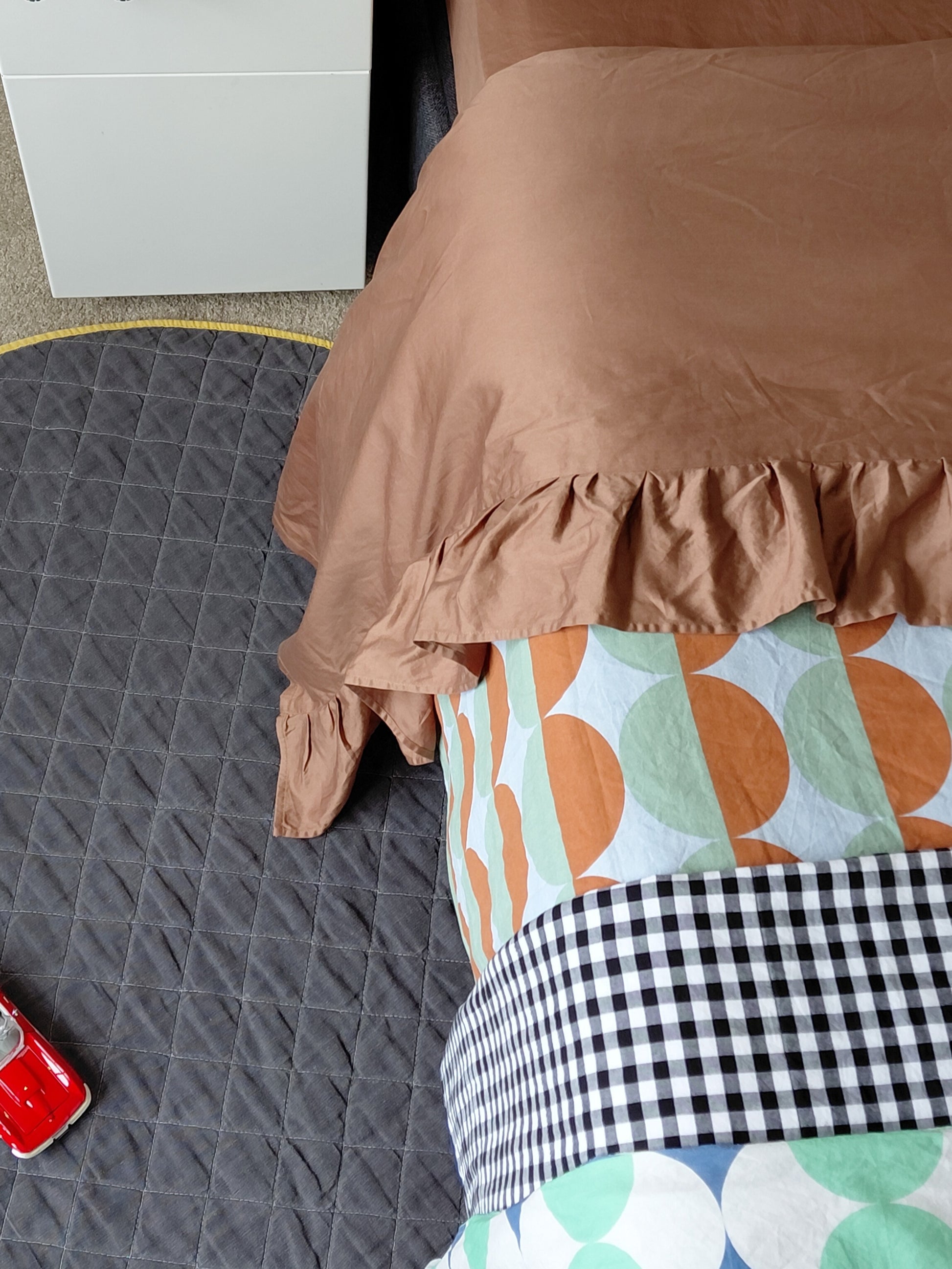 Brown chocolate top sheet with ruffle draped over a child's bed with a colorful patterned rug underneath.