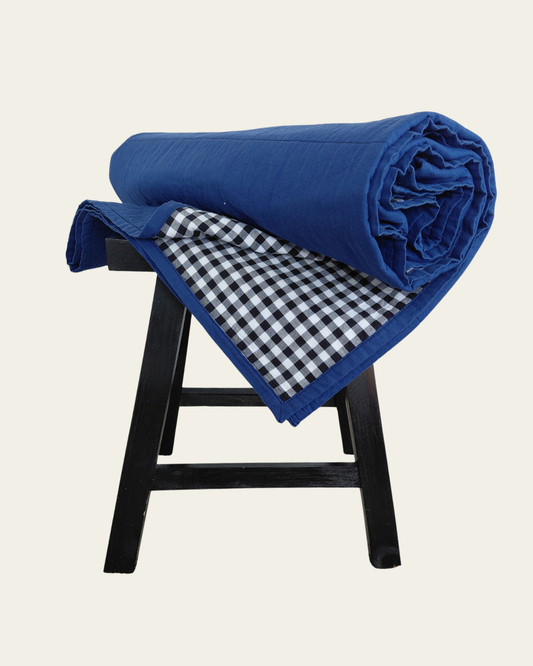 Cobalt blue blanket with checkered gingham interior on a black stool against a white background