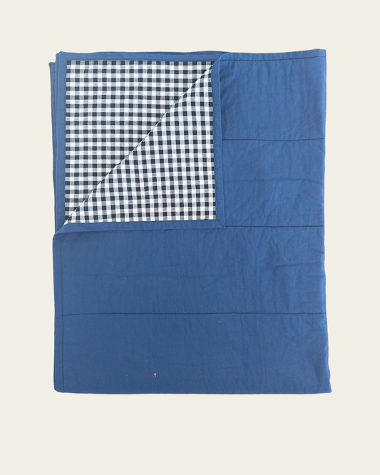 Cobalt blue cotton quilt blanket with a checkered gingham black and white pattern on a beige background