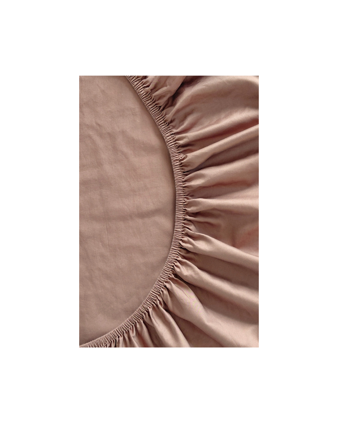 Close-up of a chocolate brown cotton fitted sheet by Small Batch Bedding with a gathered elasticized edge, shown against a white background.