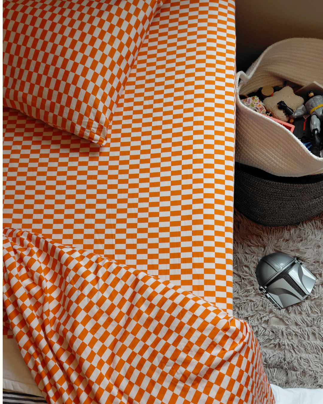 Orange and white checkered tomato tile fitted sheet with a basket of toys in the background