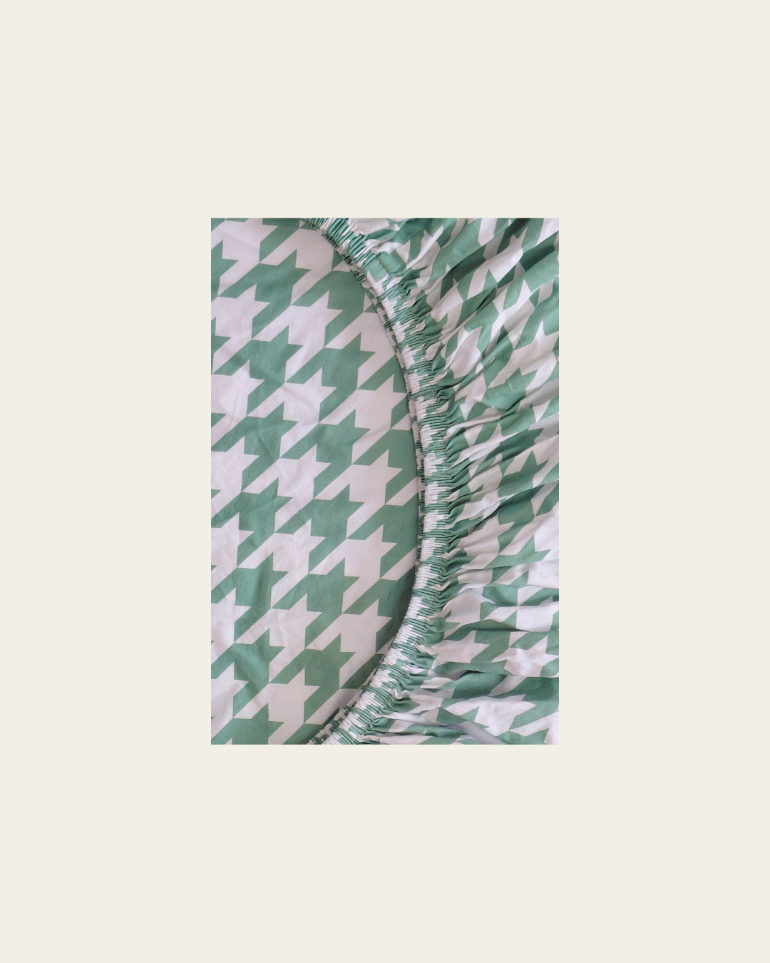 Green and white houndstooth patterned fitted cotton sheet on a beige background