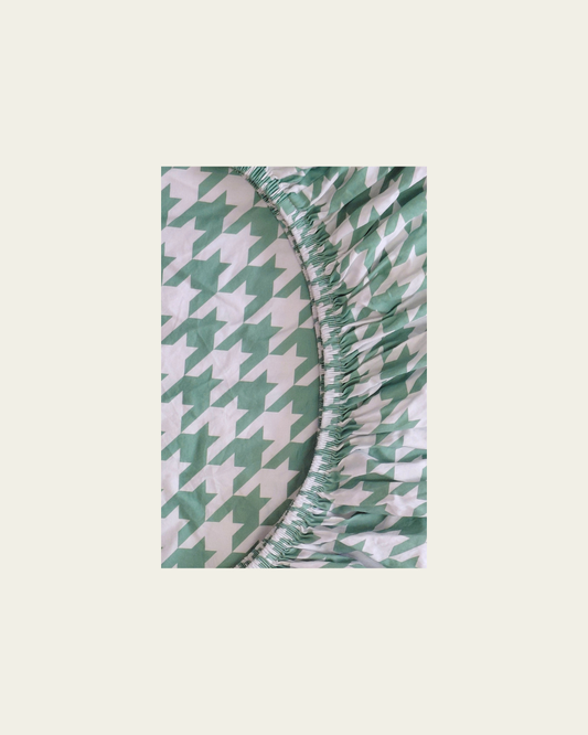 Green and white houndstooth patterned fitted cotton sheet on a beige background