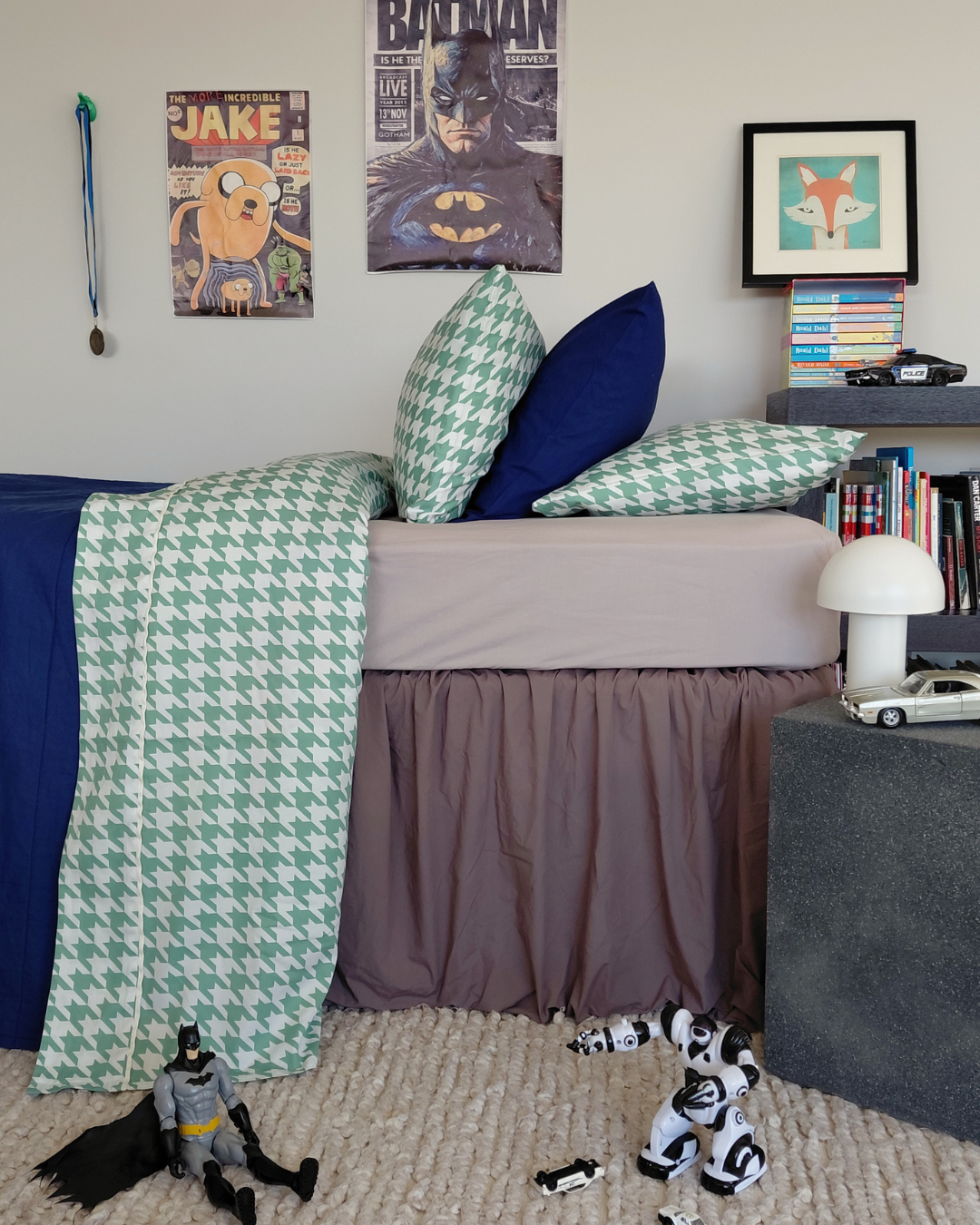Children's bedroom with bed, toys, and wall decorations featuring a green and white houndstooth top sheet and green and white houndstooth pillows.