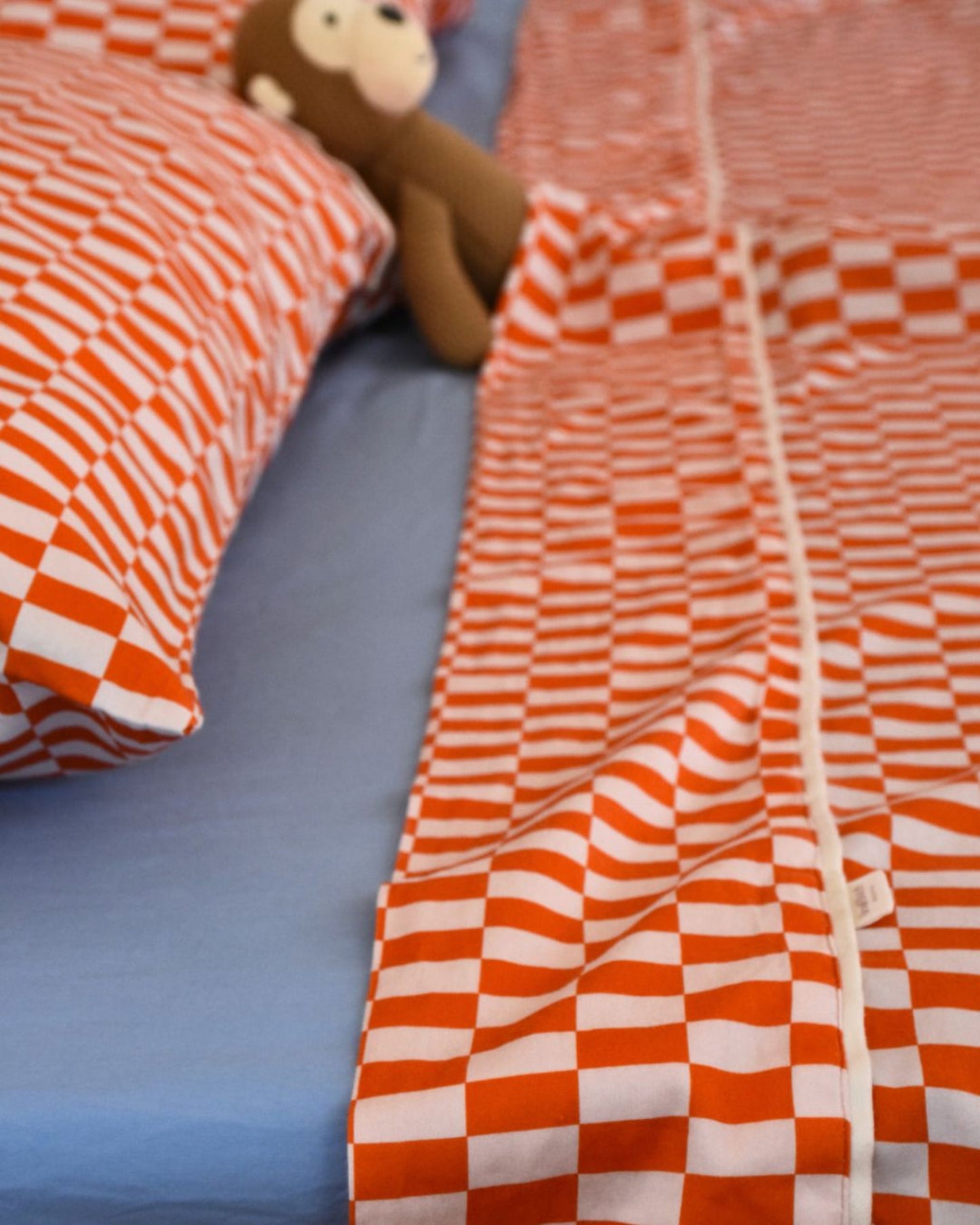 Tomato red orange and light rectangle checkered cotton kid's flat sheet with double fold and cream detail on a bed with a monkey plush toy.