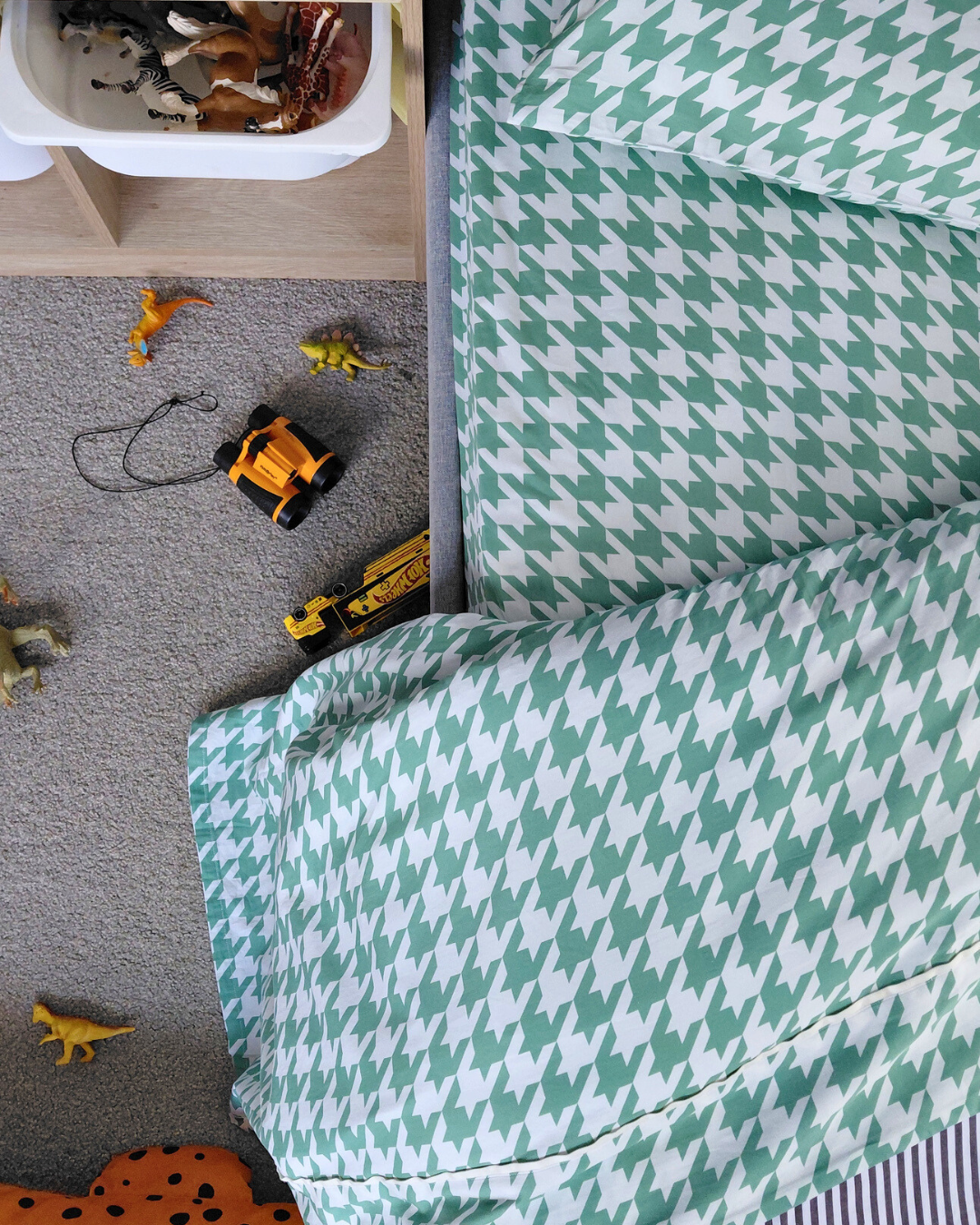 Children's room with green and white houndstooth patterned cotton sheeting, toys on the floor.