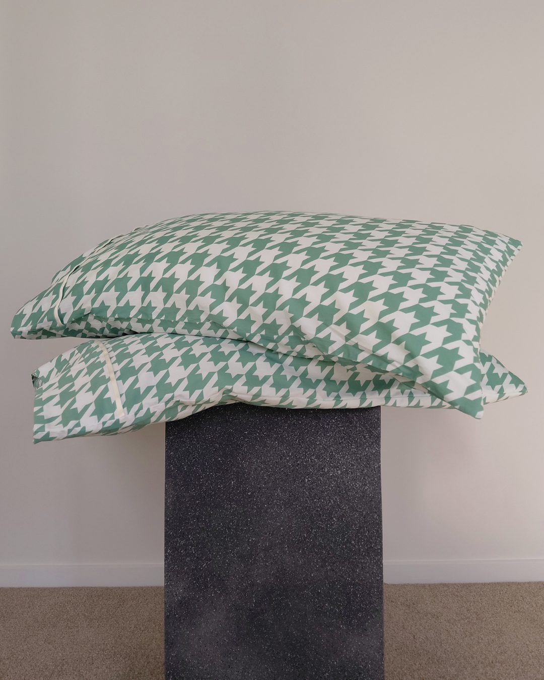 Green and white houndstooth patterned pillows on a concrete stand against a plain wall.