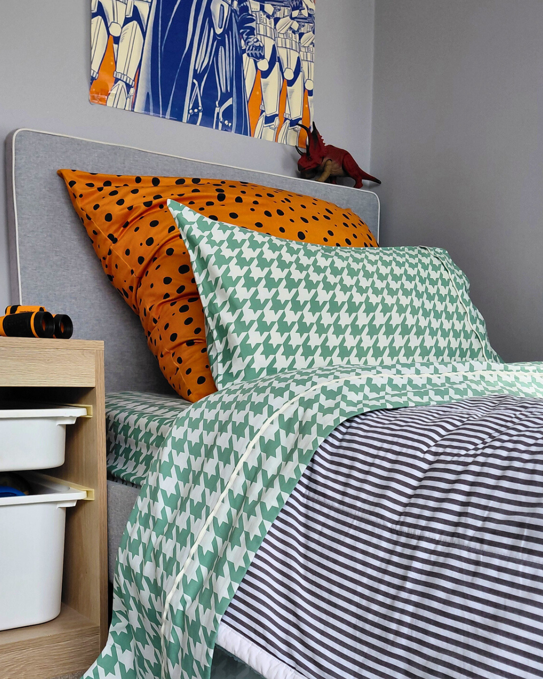 Bed with green and white houndstooth patterned bedding and pillowcase against and orange pillow.