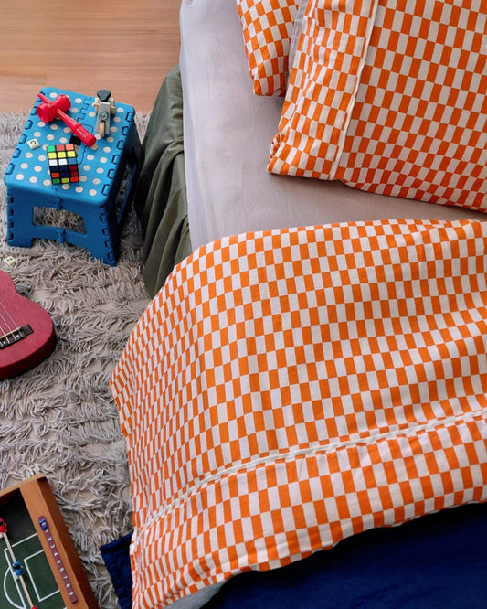 Red orange and white checkered fitted cotton sheet with matching tomato tile pillowcases on a child's bed with toys and a small table in the background