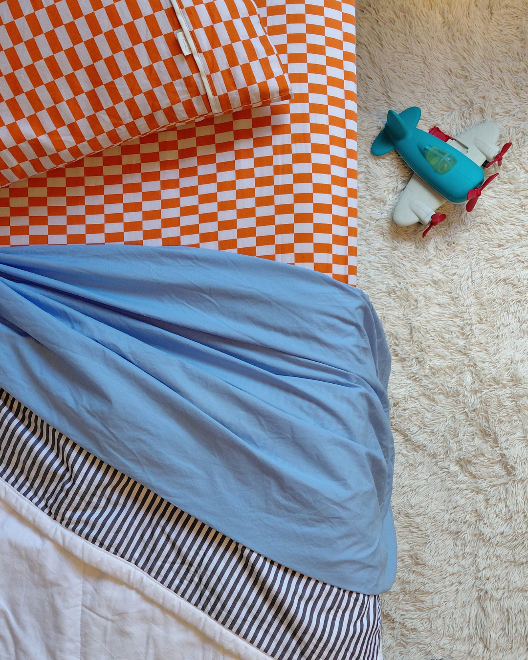 Top view of made bed with cotton white and stripe quilt blanket on a Small Batch Bedding tomato tile fitted cotton sheet and pillowcase.